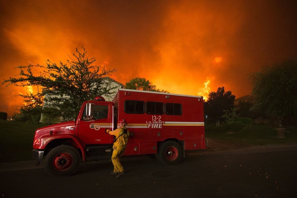 A firefighter reaches for the door of his truck as flames close in on homes at the Sand Fire on July 23 2016 near Santa Clarita, California. Fueled by temperatures reaching about 108 degrees fahrenheit, the wildfire began yesterday has grown to 11,000 acres. / AFP / DAVID MCNEW (Photo credit should read DAVID MCNEW/AFP/Getty Images)
